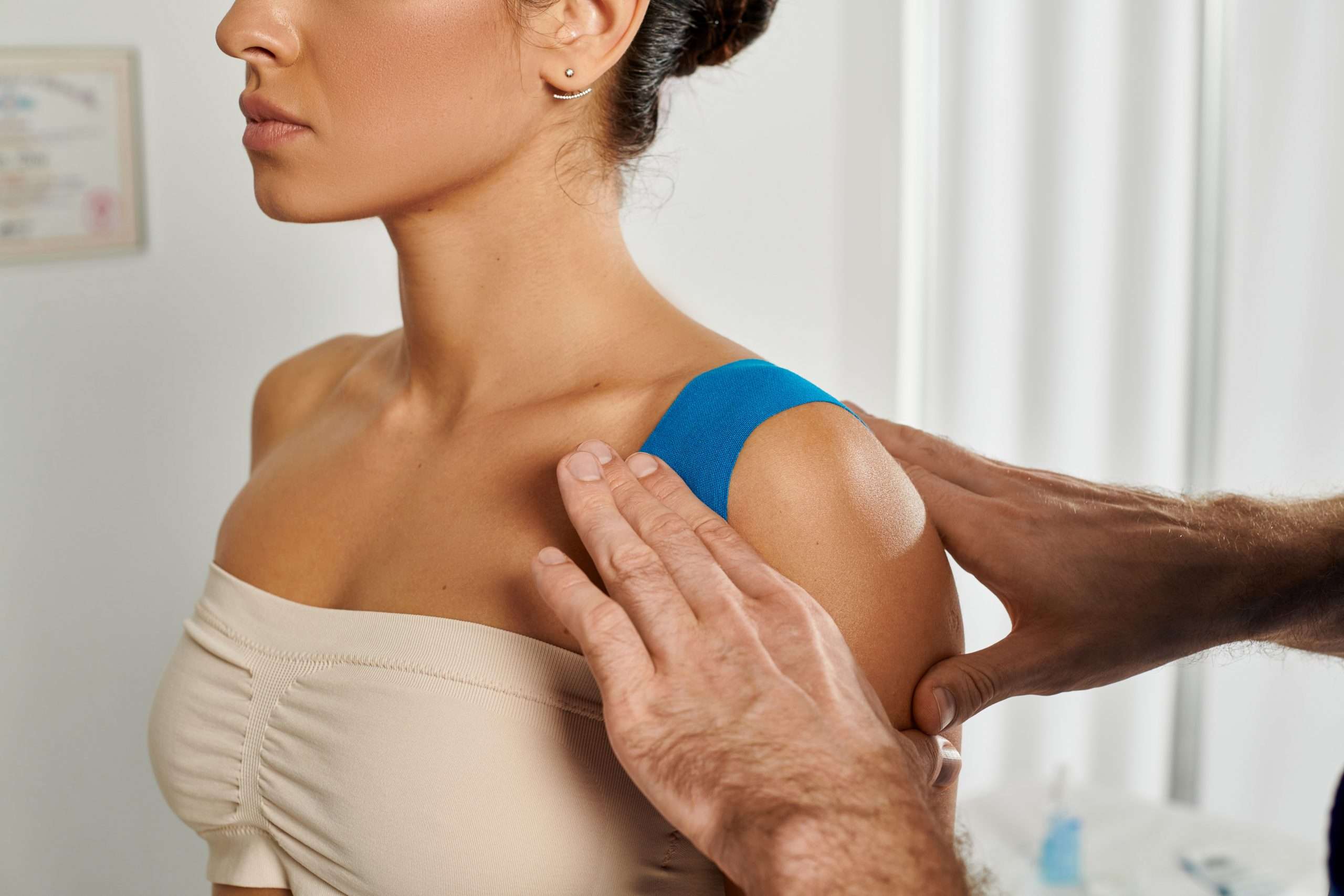 cropped view of doctor putting kinesiological tapes on his young female patient, healthcare